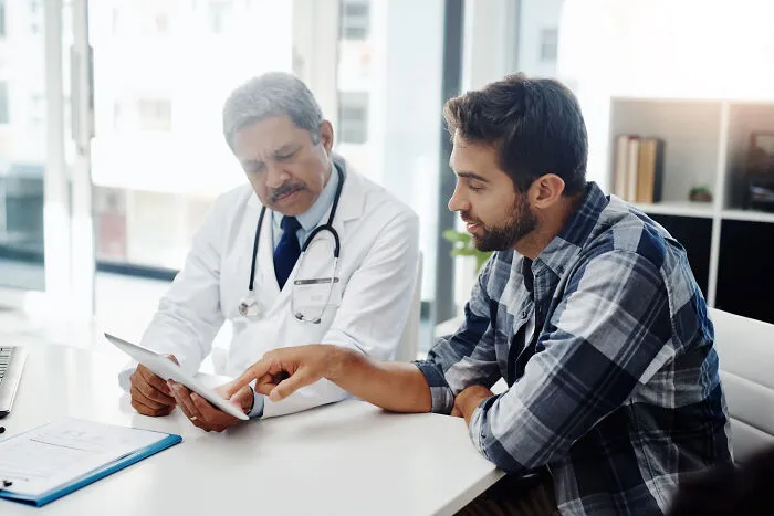 A doctor consults with a male patient, discussing his pain reactions to medical conditions.