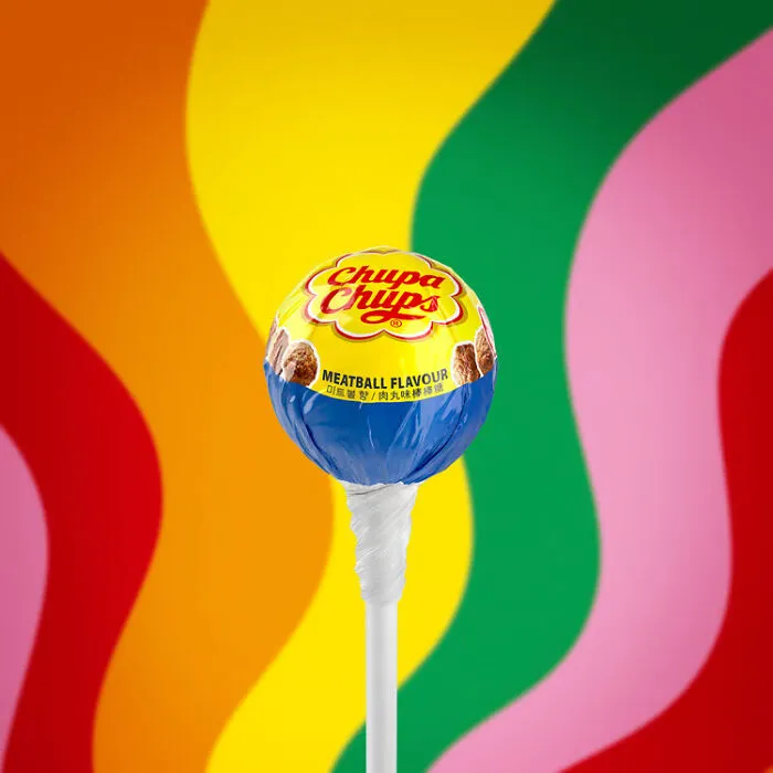 Odd food combinations featuring a meatball flavored lollipop against a colorful wavy background.