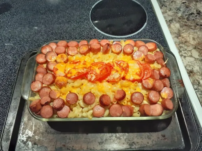 A baked macaroni dish topped with sliced hot dog rounds and tomato, representing unusual food combinations