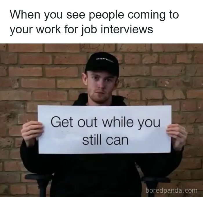 Man holding sign Get out while you still can meme about job interviews relatable to working for a living