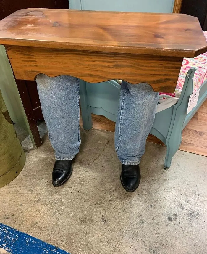 Small wooden table with mannequin legs in blue jeans and boots houses furniture.
