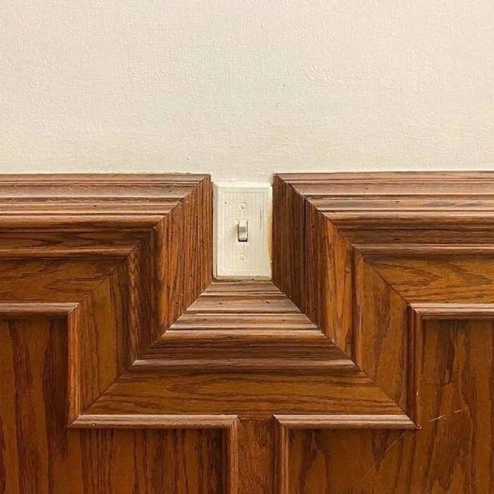 A light switch awkwardly cut into wooden paneling in a poorly planned house