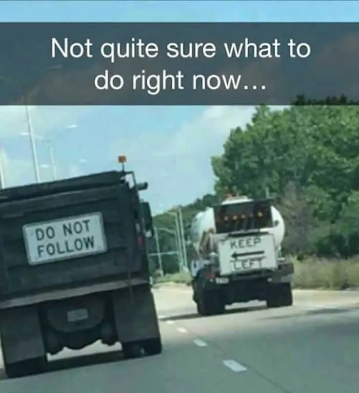 Two trucks on a road, one with a 'Do Not Follow' sign and another with 'Keep Left', creating a synced paradox.