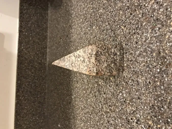 A triangular granite shelf perfectly synced in texture and color with a speckled gray wall.