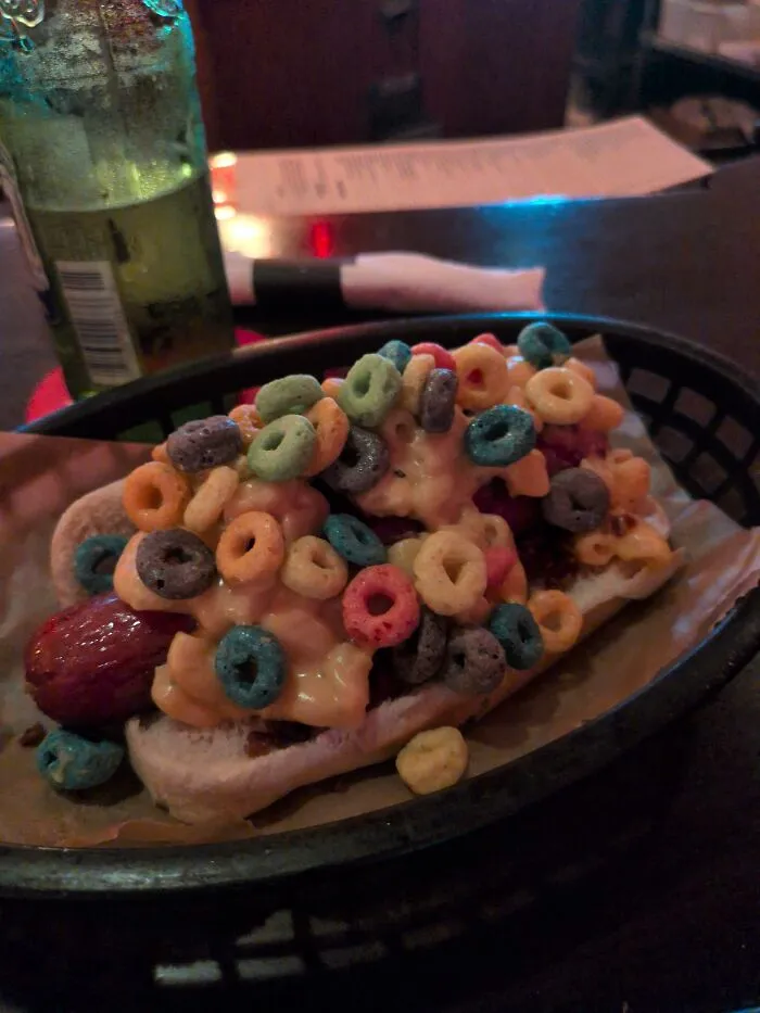 Unusual food combinations of a hot dog topped with mac and cheese and colorful cereal