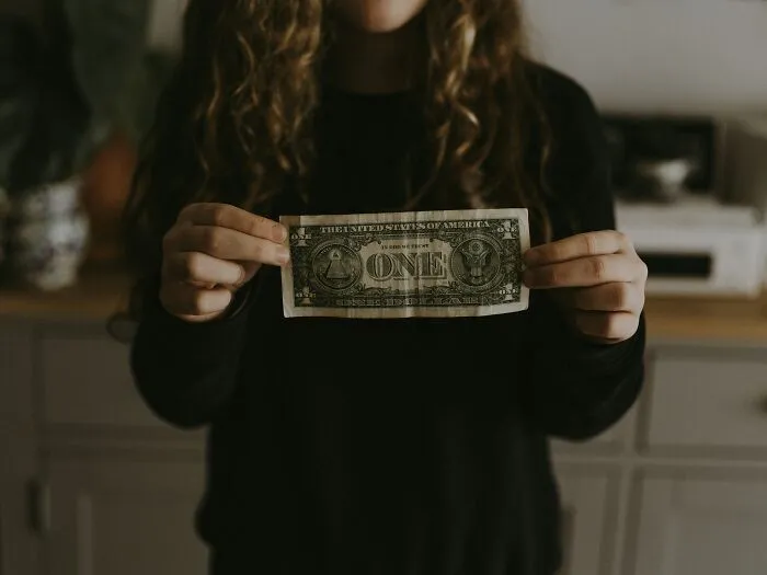 A person holding a one-dollar bill, illustrating the financial strain in a difficult job market.