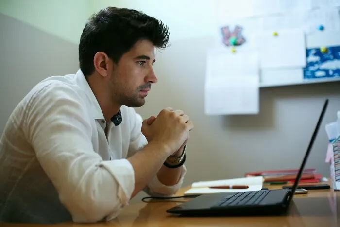 A concerned man sitting at his desk looking at his laptop, symbolizing the tough job market.