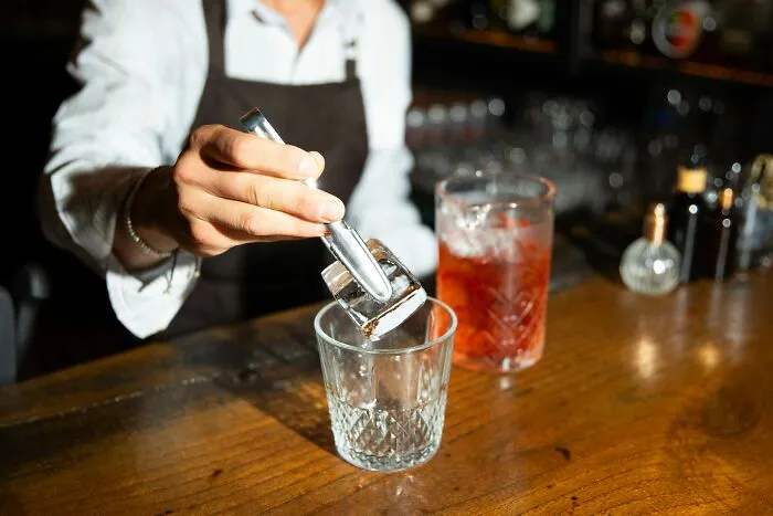 A bartender placing an ice cube into a glass, highlighting the competitive job market for hospitality workers