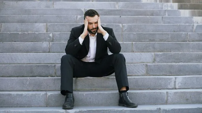 A stressed man in a suit sitting on stairs, reflecting the struggles of being unemployed in today's job market
