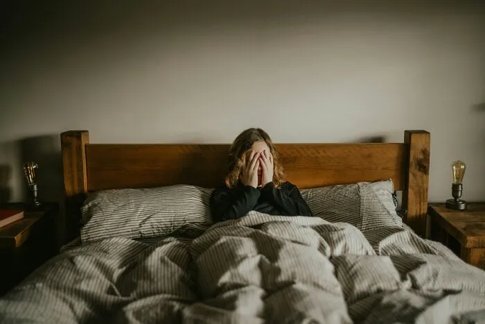 An anxious person covering their face in bed, reflecting a tough job market.