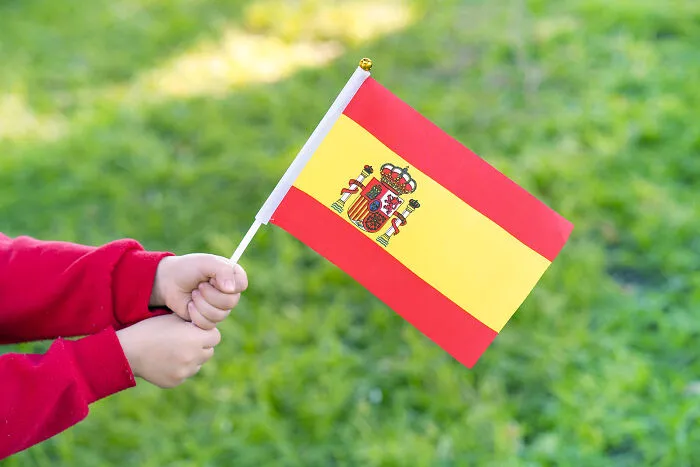 Child holding a small Spanish flag with blurred greenery background