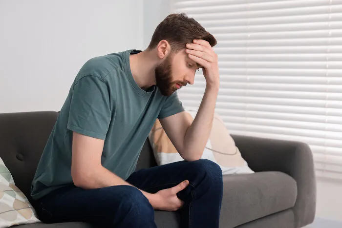 A disappointed man sitting on a sofa with his hand on his head, expressing deep marriage regrets