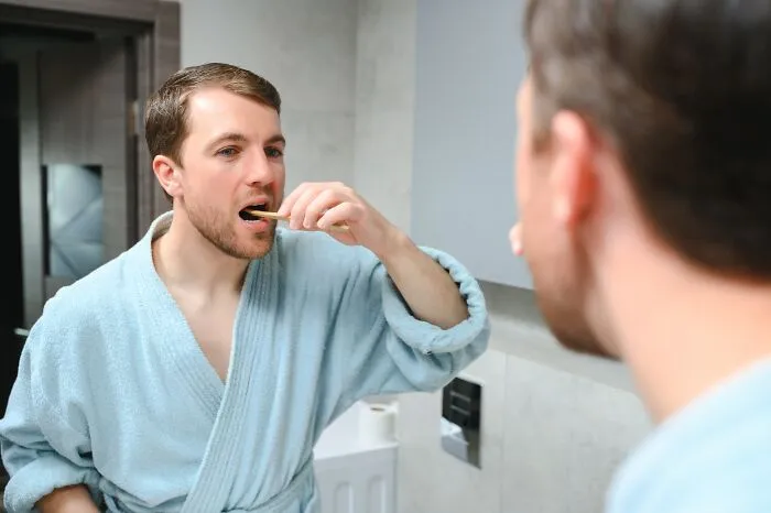 Man in bathrobe brushing teeth in front of bathroom mirror