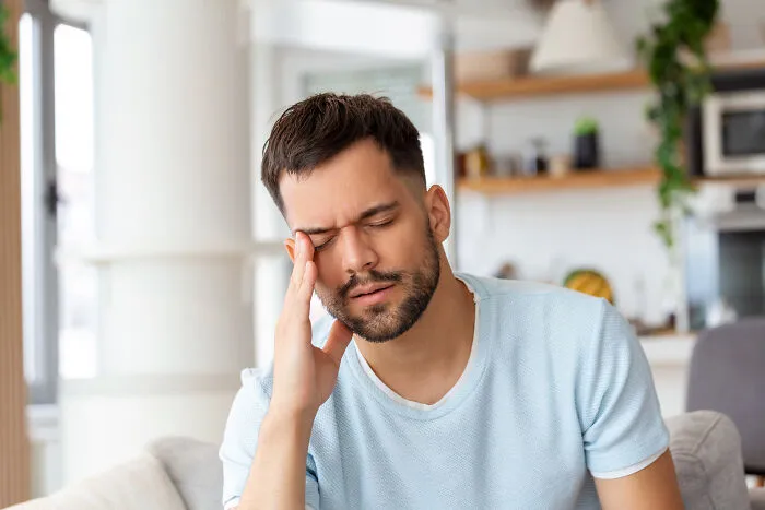 Stressed man touching temple with closed eyes in home setting