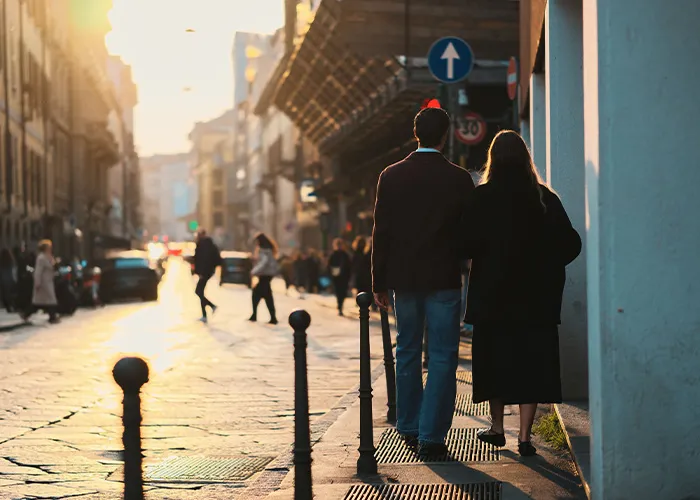 A couple strolling arm in arm down a city street at sunset, showing how men should treat women attentively.