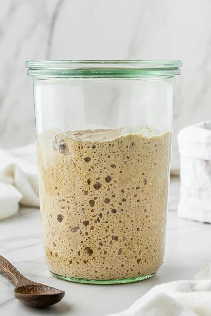 A glass jar filled with active sourdough starter mixture
