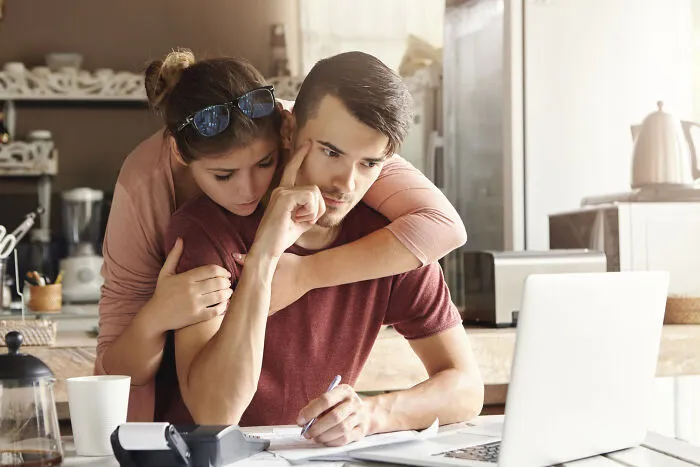 Woman hugging stressed man working on laptop, showing toxic relationship signs