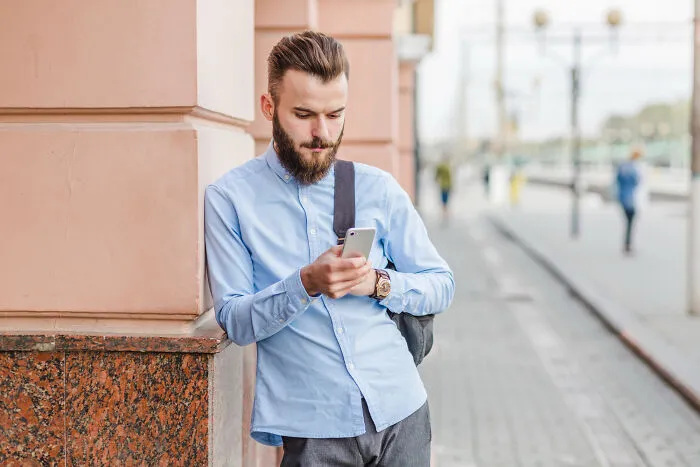 Young man checking phone outside urban building, symbolizing ex-boyfriend toxicity