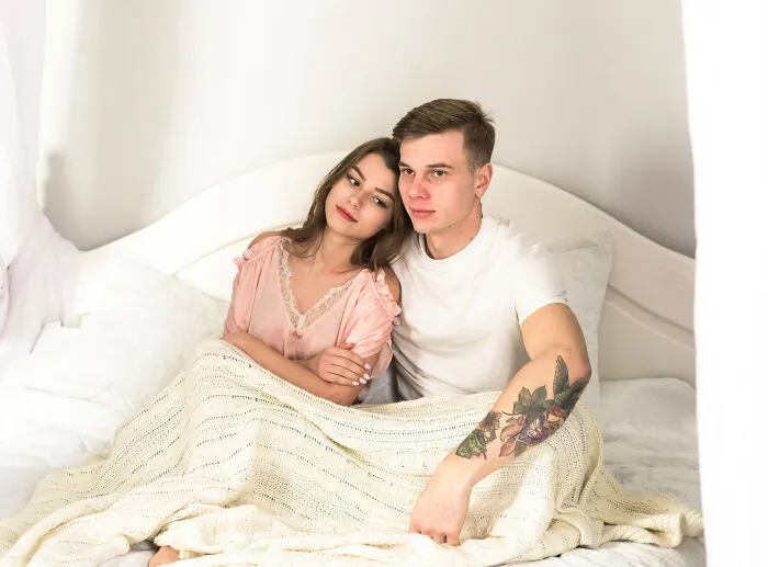 Young couple sitting close in bed wrapped in a blanket showing intimacy