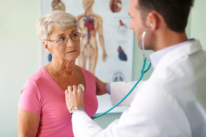A medical worker listening to a senior patient's heartbeat with a stethoscope.