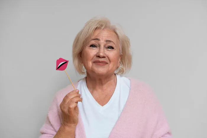 A senior woman holding a paper lips prop on a stick next to her face.