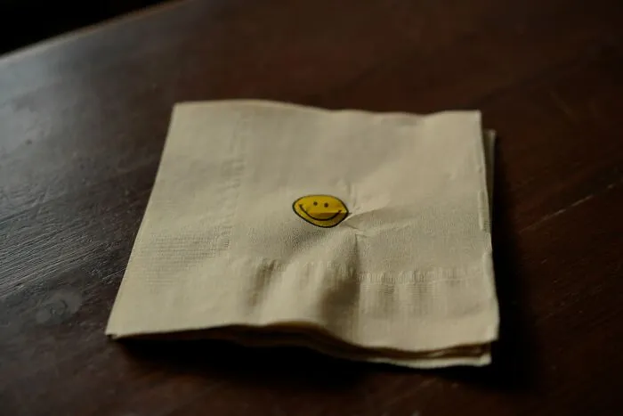 A simple paper napkin with a small yellow smiley face, representing sweet patient stories.