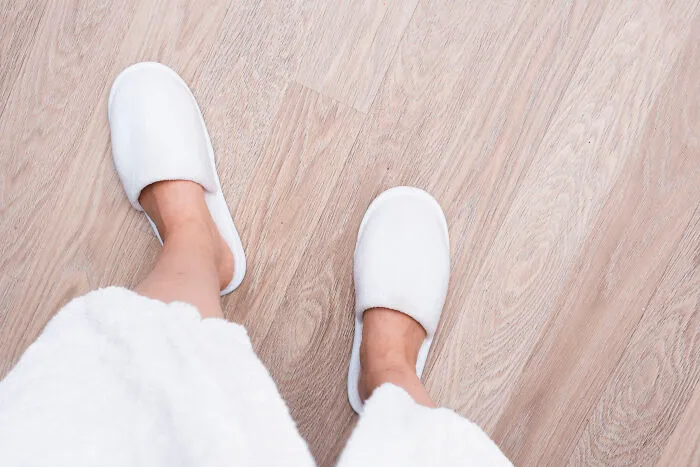 A patient wearing white slippers and a robe standing on a wooden floor, sharing patient stories