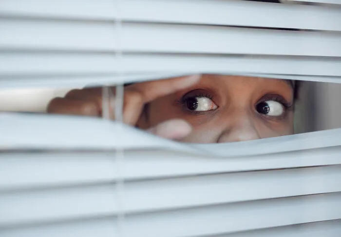 A pair of eyes peeking curiously through white window blinds, representing medical workers observing patients