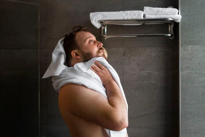 Man drying off with white towel in a bathroom with towels hanging