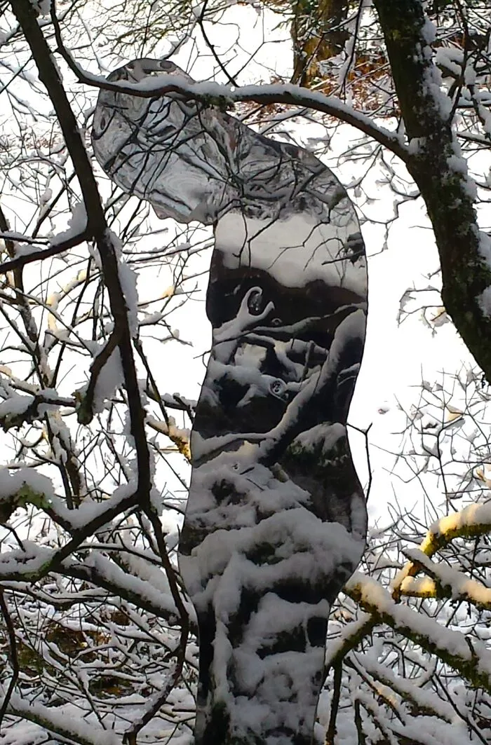 Snow-covered reflective sculpture mirroring winter trees