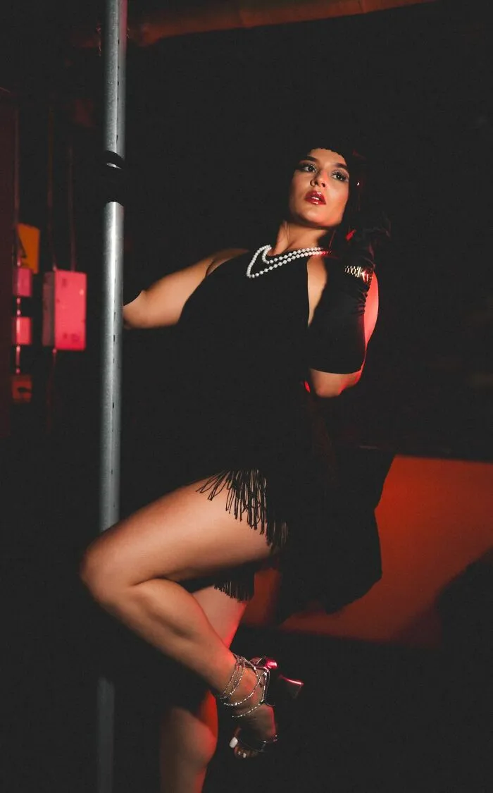 A woman in a black flapper dress and pearls posing next to a pole. This image illustrates legal excuses.