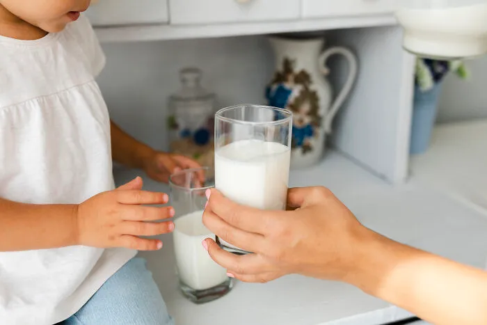 An adult hand offering a glass of milk to a young child, depicting cheap and healthy nutrition.