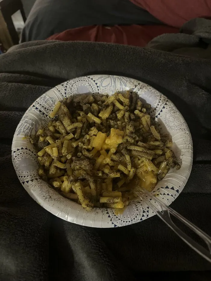 A paper bowl of mac and cheese heavily coated with black pepper, illustrating unusual food combinations