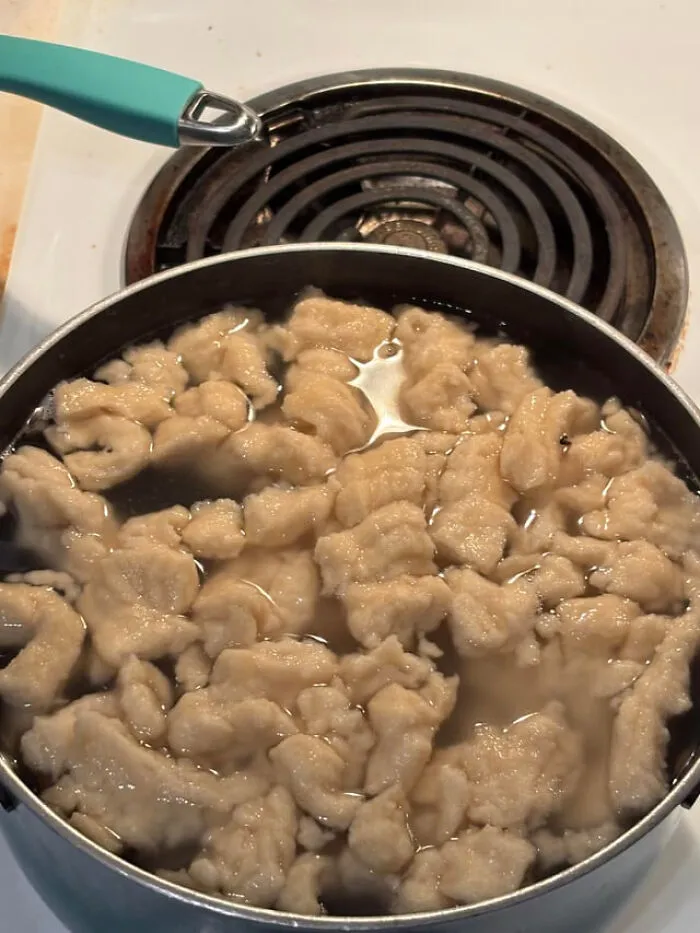 Fluffy boiled dough shapes cooking in a pot of water as part of unique food combinations.