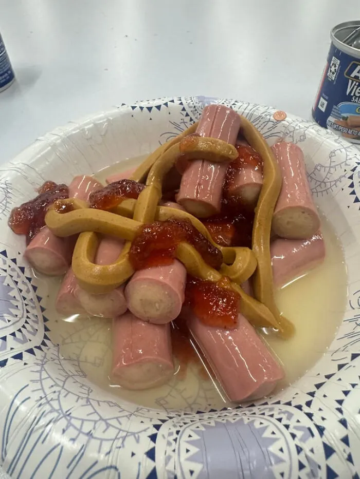 Strange food combination of sliced hot dogs covered in peanut butter and jam on a paper plate