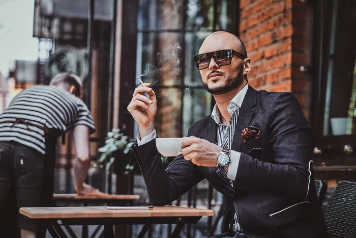 A stylish man with sunglasses smoking and drinking coffee at an outdoor cafe, showing various life paths.