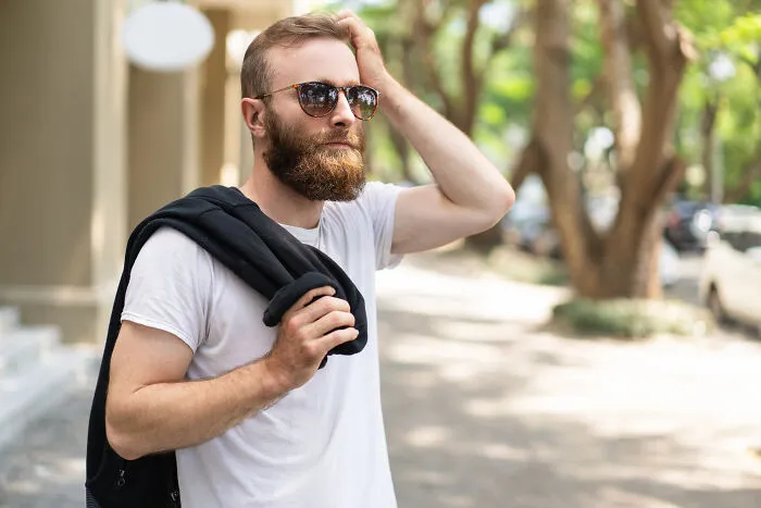 Man wearing sunglasses outdoors with jacket over shoulder