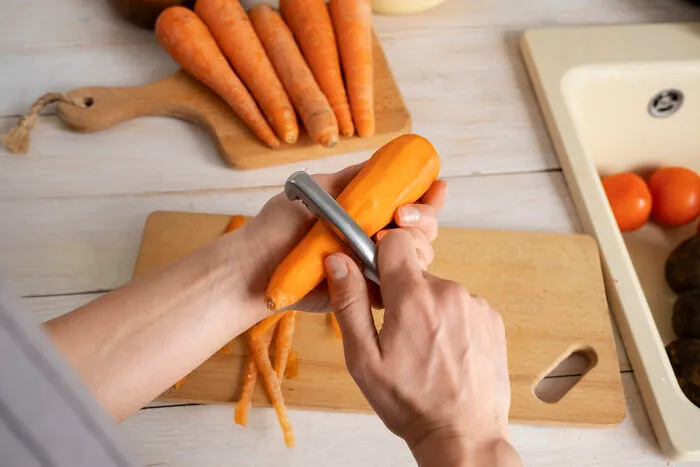 Hands peeling a fresh carrot on a cutting board in a kitchen