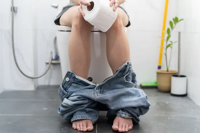 Person sitting on toilet holding toilet paper roll in bathroom