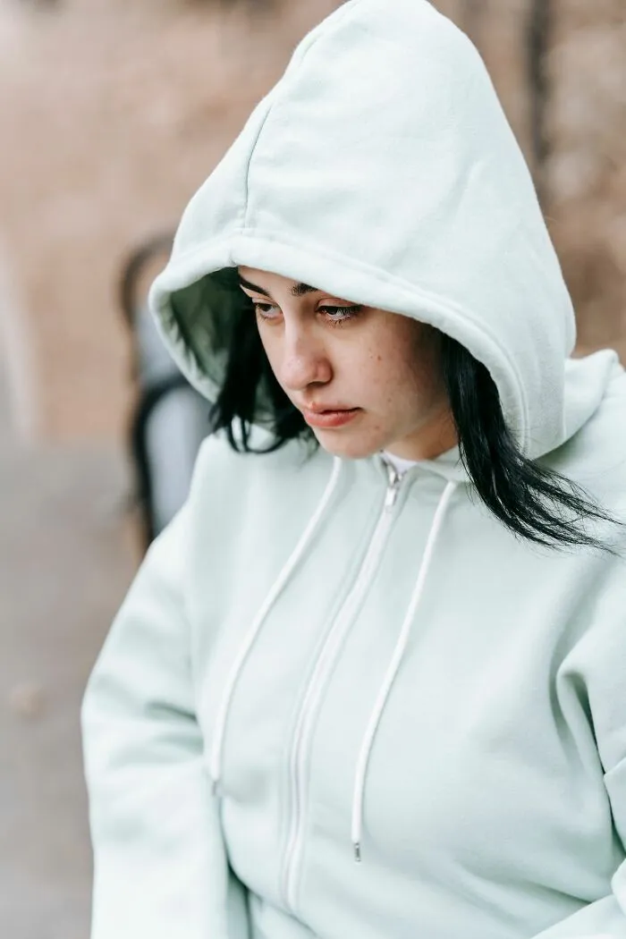 A young woman in a light hoodie looks down, symbolizing children who are going through difficult experiences.