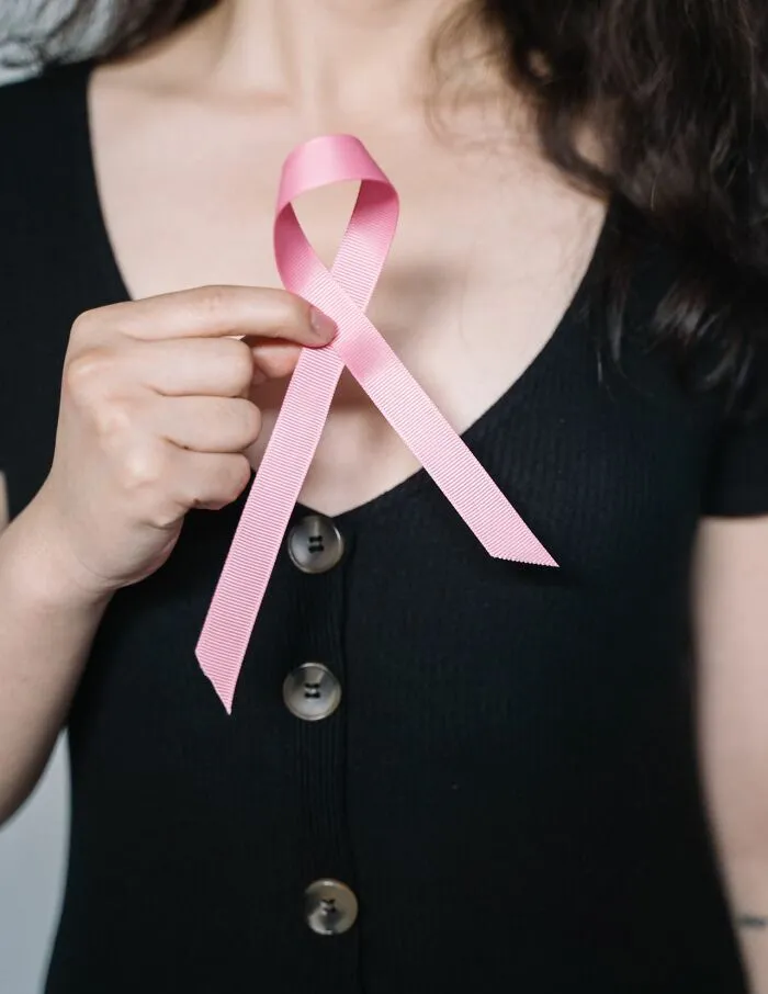 A woman holding a pink ribbon close to her chest, symbolizing useful facts about health awareness.