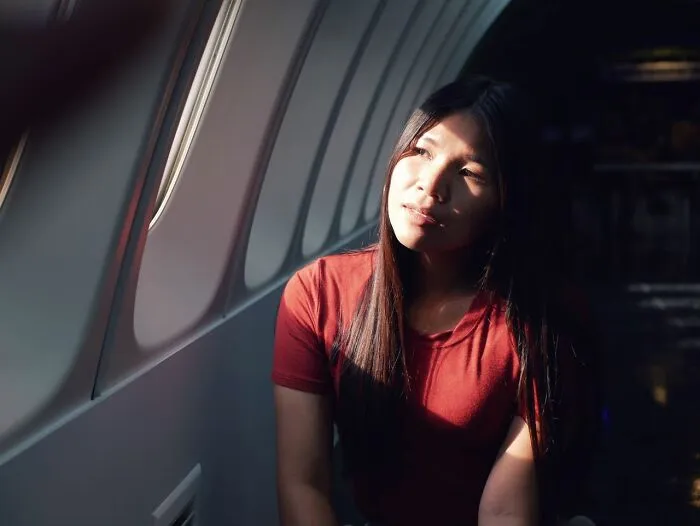 A young woman in a red shirt looking out the window while sitting next to a plane seatmate on a flight.