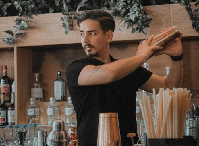 A professional bartender shaking a drink behind the bar, representing scandals in the service industry