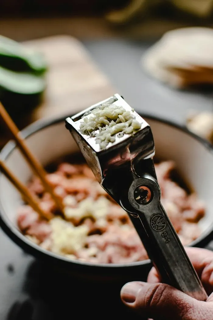 A hand holding a garlic press with freshly crushed garlic, a kitchen detail of middle-class life