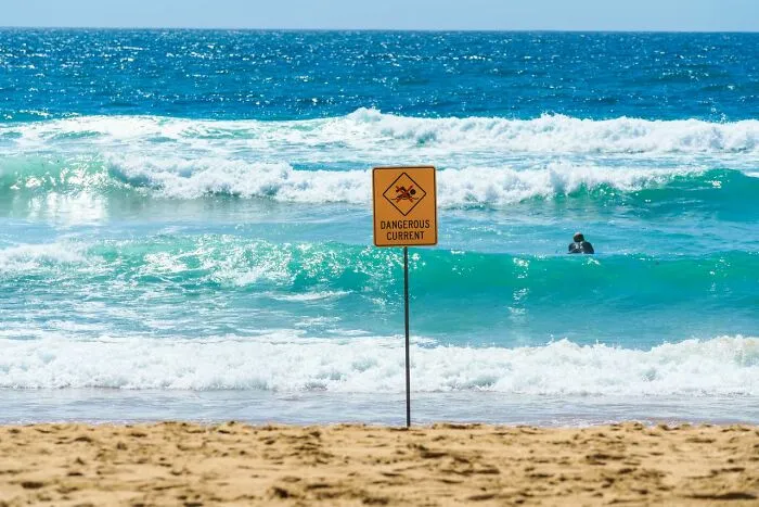 Yellow warning sign for dangerous currents on a sandy beach, highlighting essential safety facts in an emergency.