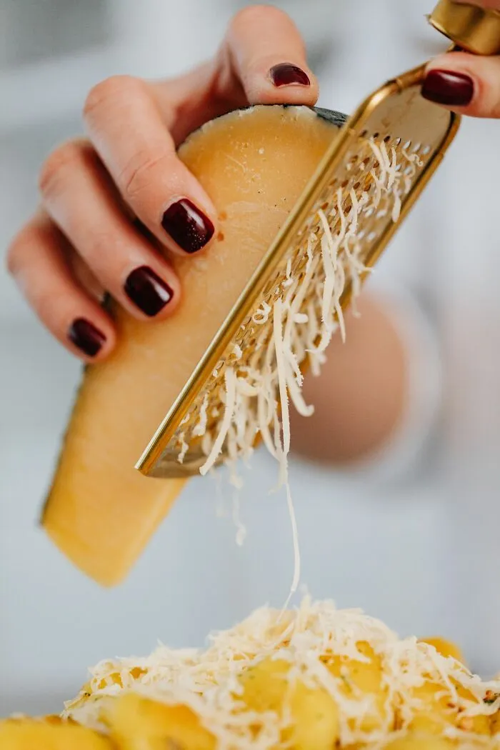 A close-up of a person grating fresh cheese over a dish, a common scenario in middle-class life.