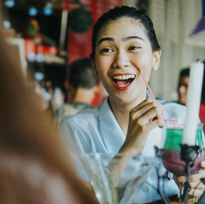 Woman laughing and drinking colorful cocktail at restaurant enjoying funny moment