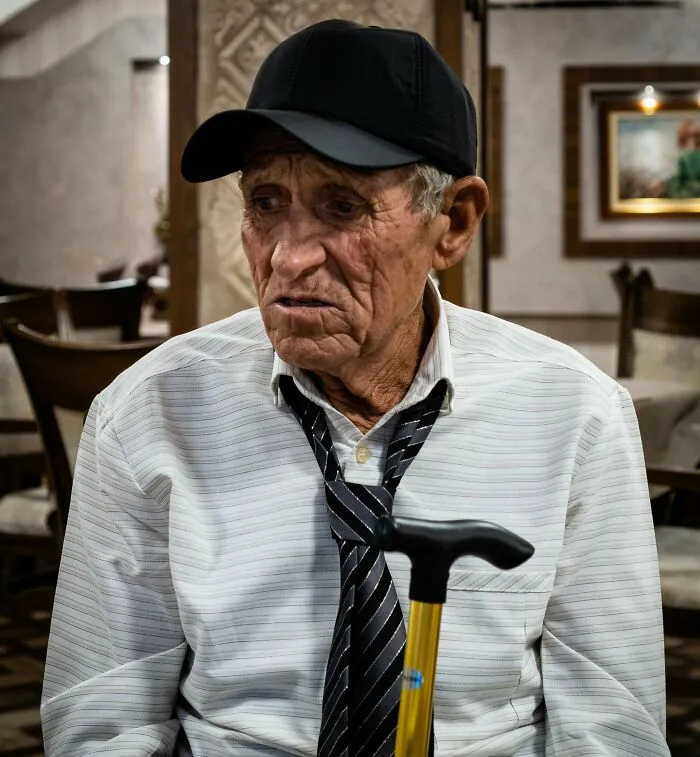 Elderly man with cane and hat sitting in restaurant looking sideways