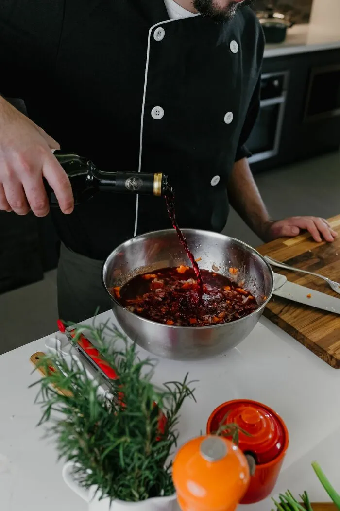 Chef pouring red wine into a metal mixing bowl, symbolizing gourmet cooking in a middle-class life