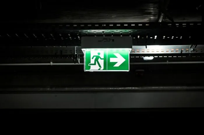 An illuminated green exit sign in a dark corridor indicating emergency evacuation direction.